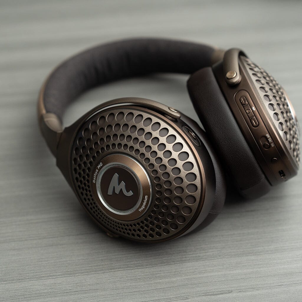 The Focal Bathys MG Wireless Headphones by Focal, featuring a perforated outer design and visible control buttons, are displayed on a light gray surface.