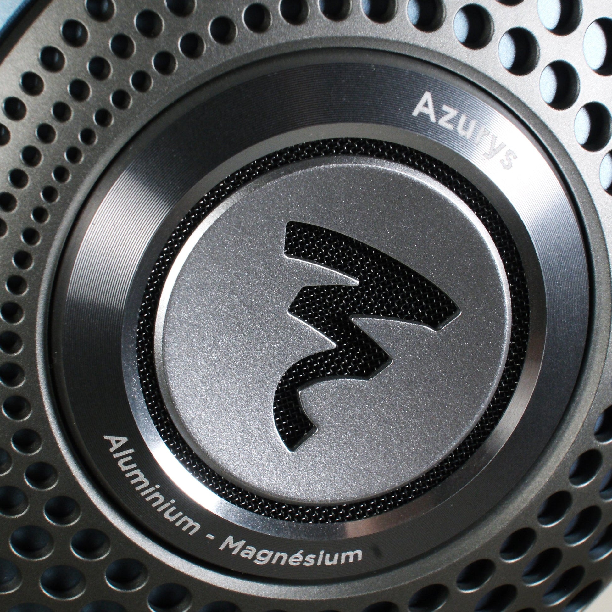 Close-up of a Focal Azurys headphone earcup with a perforated design, displaying the Azurys name and Aluminium - Magnésium text encircling Focals stylized logo at the center.
