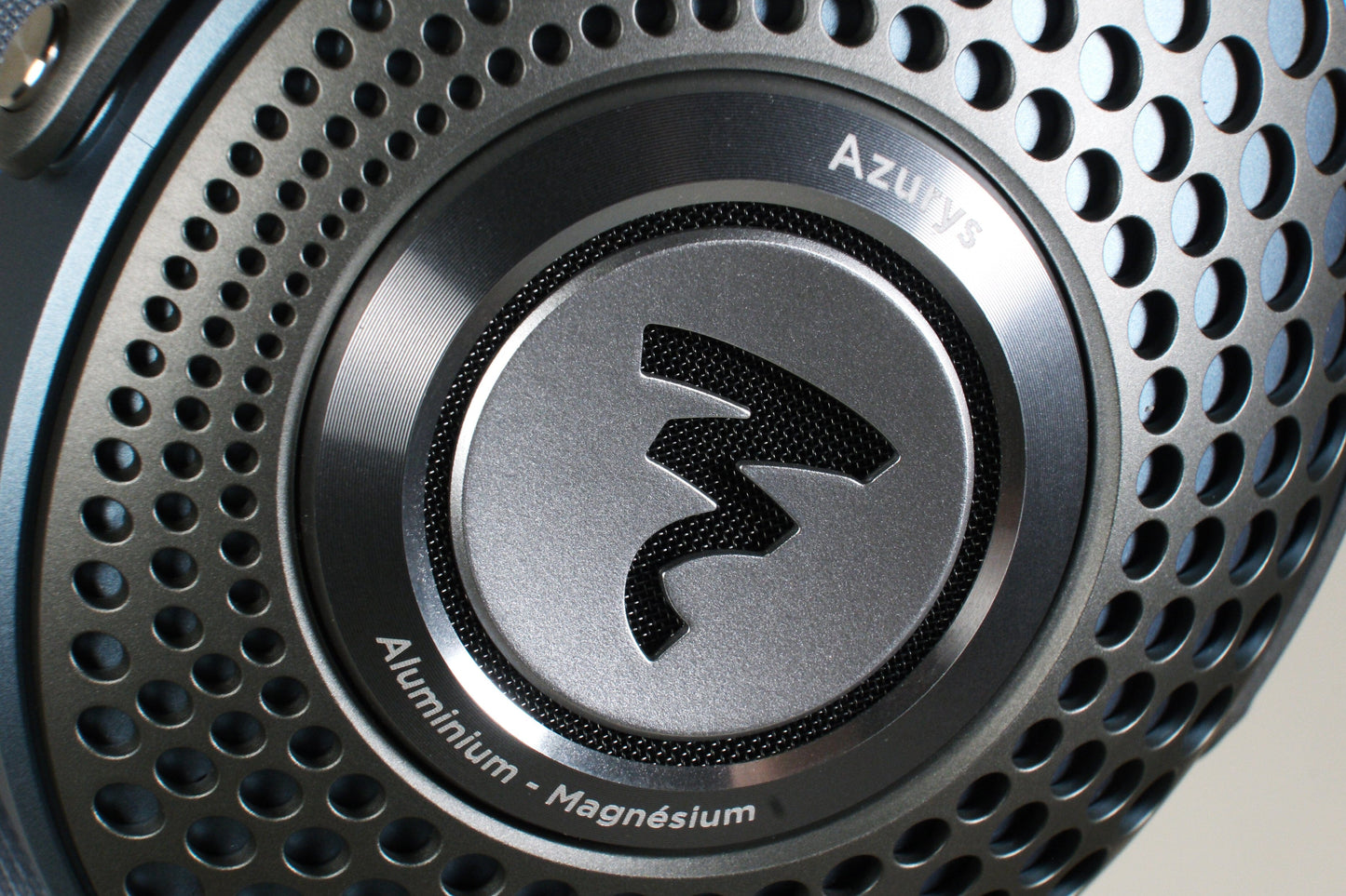 Close-up of a Focal Azurys headphone earcup with a perforated design, displaying the Azurys name and Aluminium - Magnésium text encircling Focals stylized logo at the center.
