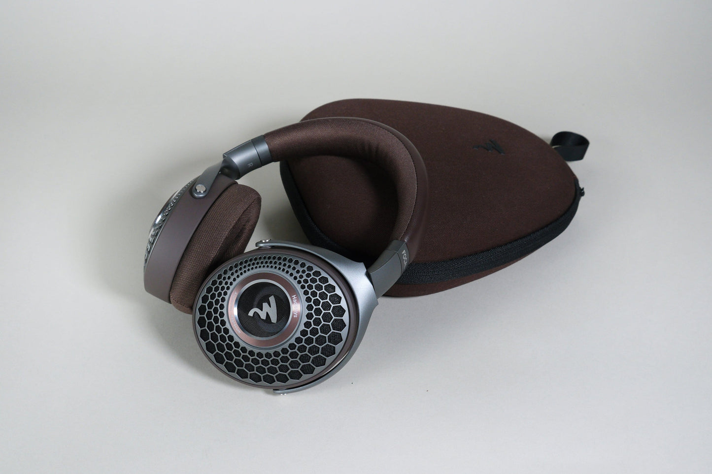 A pair of Focal Hadenys headphones by Focal, featuring Aluminium/Magnesium drivers, rests on a matching brown zippered carrying case against a plain light background.