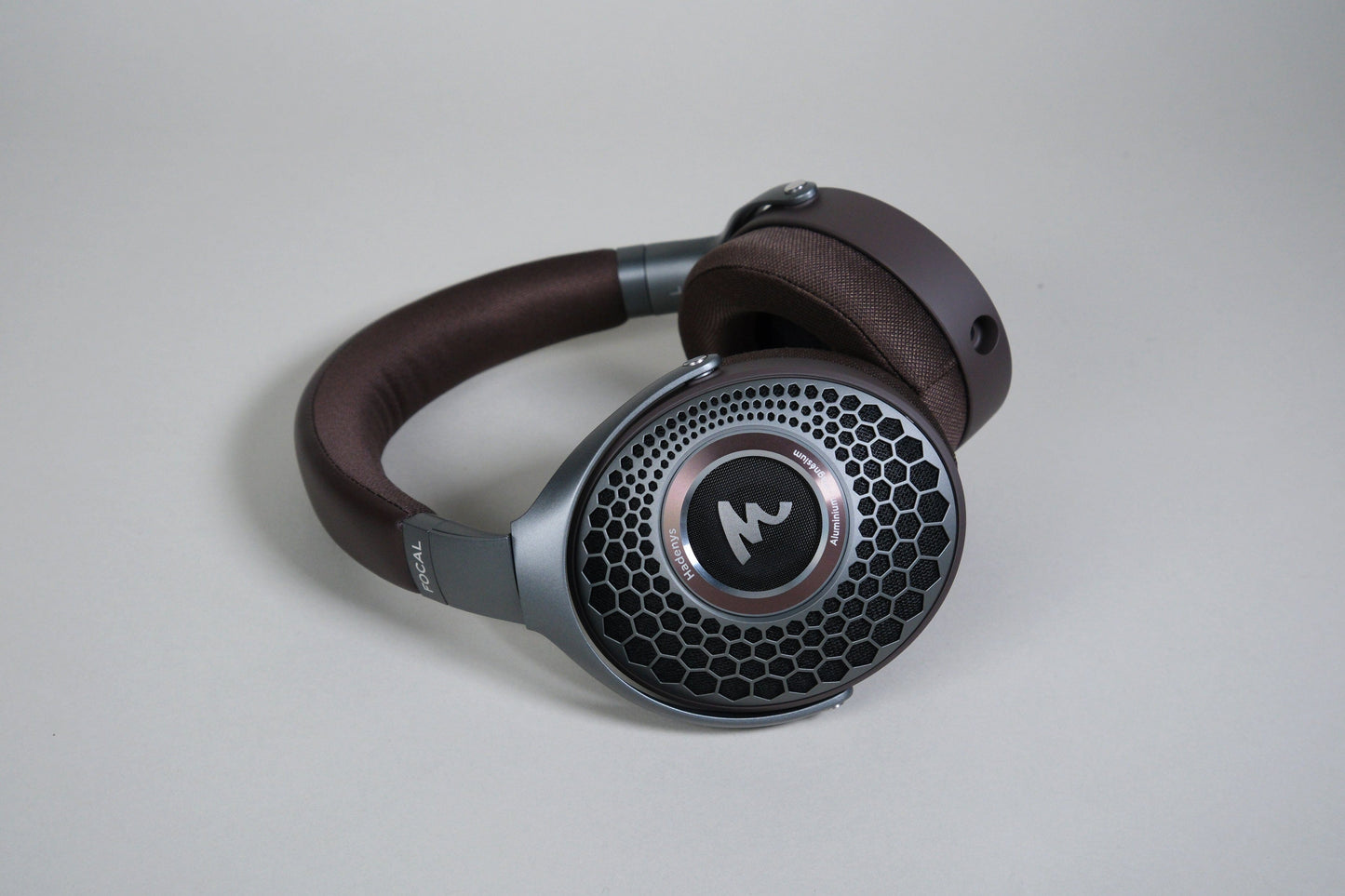 Focal Hadenys headphones by Focal feature a brown headband, black and silver honeycomb open-back ear cups, a stylish M logo, and premium Aluminium/Magnesium drivers for dynamic sound.
