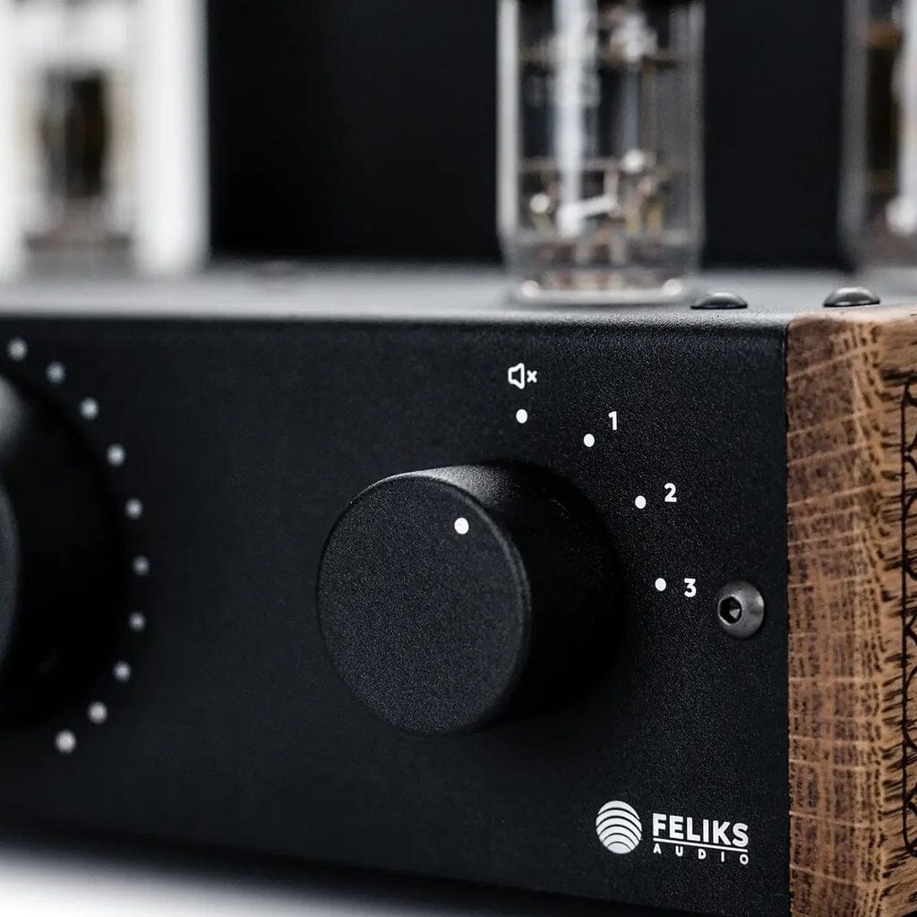 Close-up of the Feliks Audio Echo Vibe Headphone Tube Amplifier, showcasing wooden side panels, a large volume knob, a smaller numbered knob, the Feliks Audio logo, and vacuum tubes rising elegantly in the background.