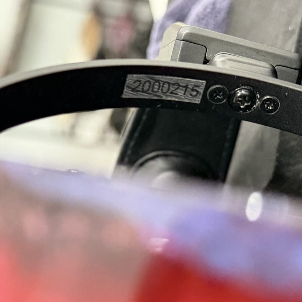 Close-up of a black component with a metallic label marked "200215" and two visible screws, likely part of the Rosson Audio Design RAD-0 Headphones (Open Box C Condition - Clearance - 215). The background is blurred, showing indistinct colors and shapes.