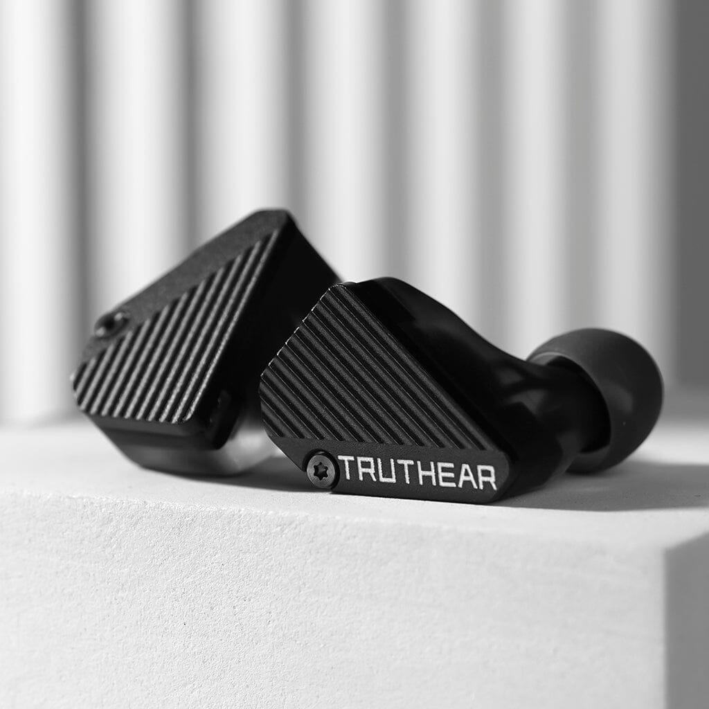 Close-up of black TRUTHEAR Truthear Pure In-Ear Headphones with a ridged texture and hybrid 4-driver setup, resting on a white surface against a blurred striped background.