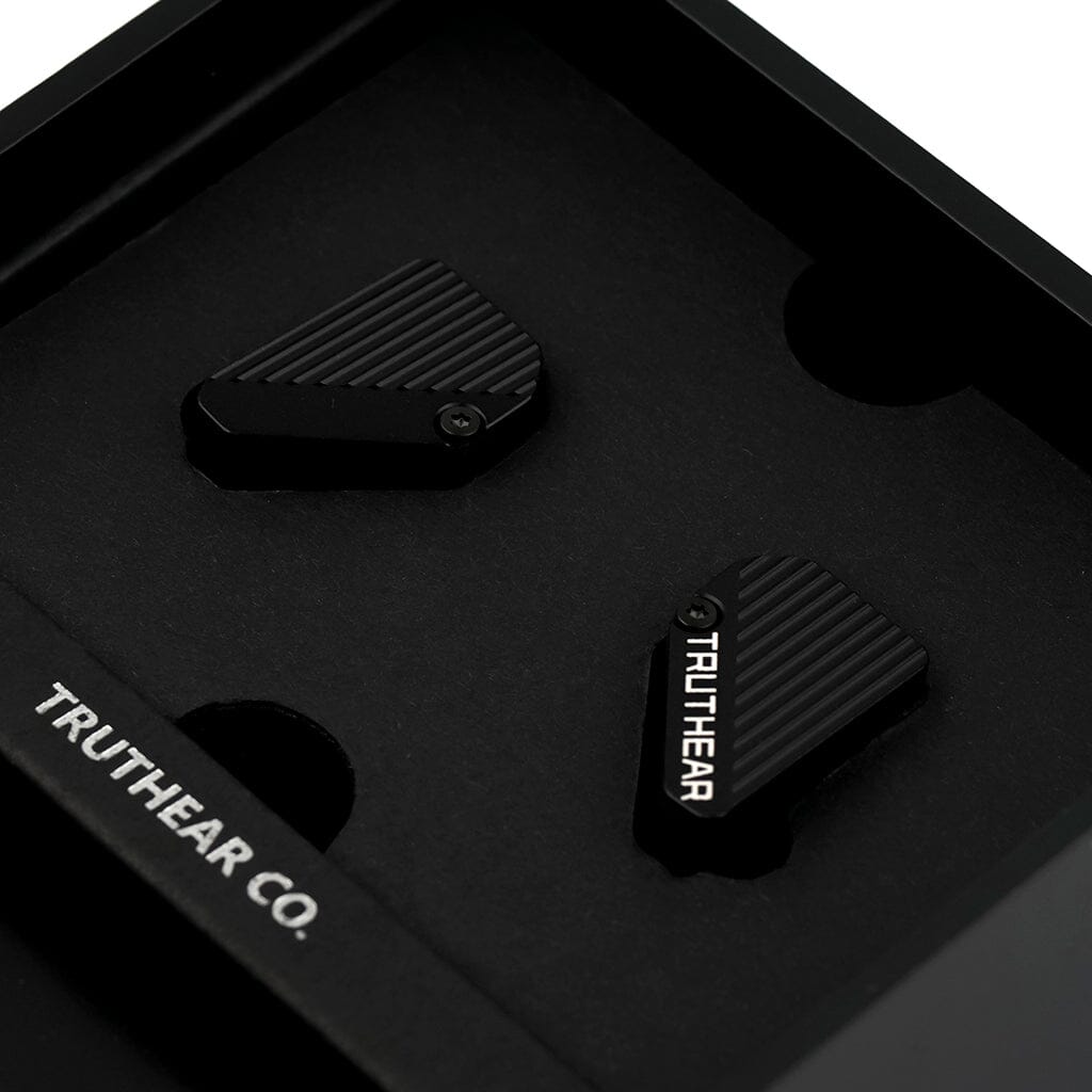 A close-up of two black, angular TRUTHEAR Pure In-Ear Headphones with diagonal grooves rests in a foam insert inside a black box, one marked with TRUTHEAR, showcasing their hybrid 4-driver design and outstanding sound quality.