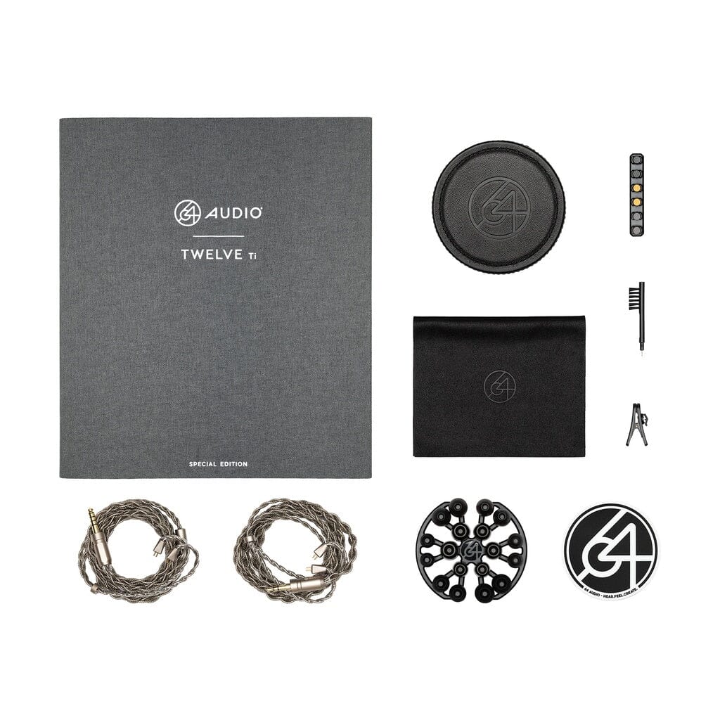 Flat lay of the 64 Audio TWELVE Ti In-Ear Headphones by 64 Audio, showing a grey box, two cables, carrying case, cleaning brush, pouch, cable organizer, sticker, and remote control arranged on a white background.