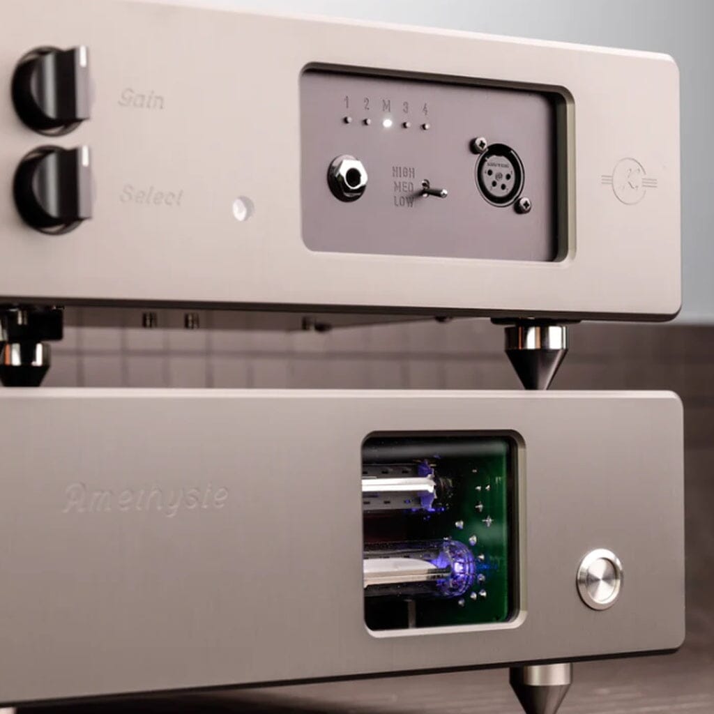 Two silver Kallyste audio devices are stacked. The top unit, the Kallyste Amethyste Reference Headphone Amplifier, features knobs, switches, and a dial, while the bottom device is a tube preamplifier with a window revealing blue-glowing tubes inside. Both showcase Class A/B output power in a sleek, modern design.