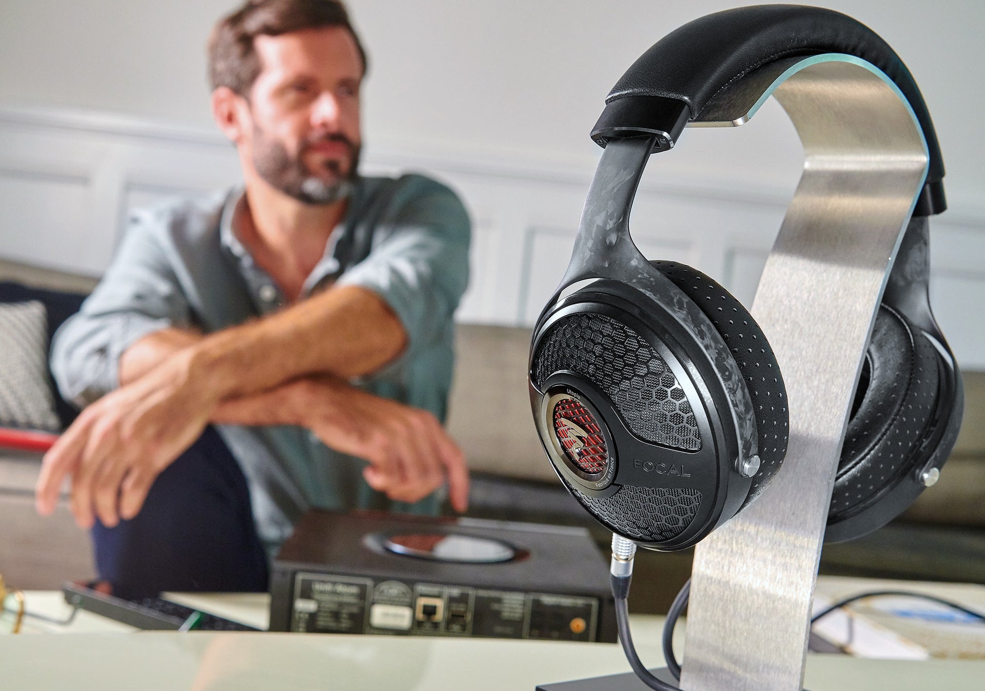 Utopia headphones on metal stand with sitting man in background