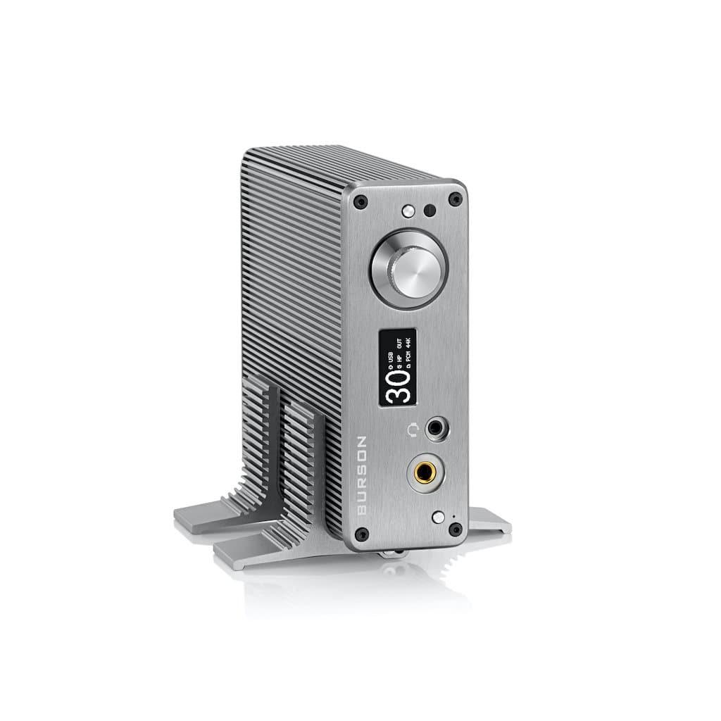 The Burson Audio Playmate 2 by Burson Audio is a sleek metallic audio amplifier featuring a ribbed vertical heatsink, large control knob, digital display, DAC input ports, and the brand logo on the front, set against a white background.