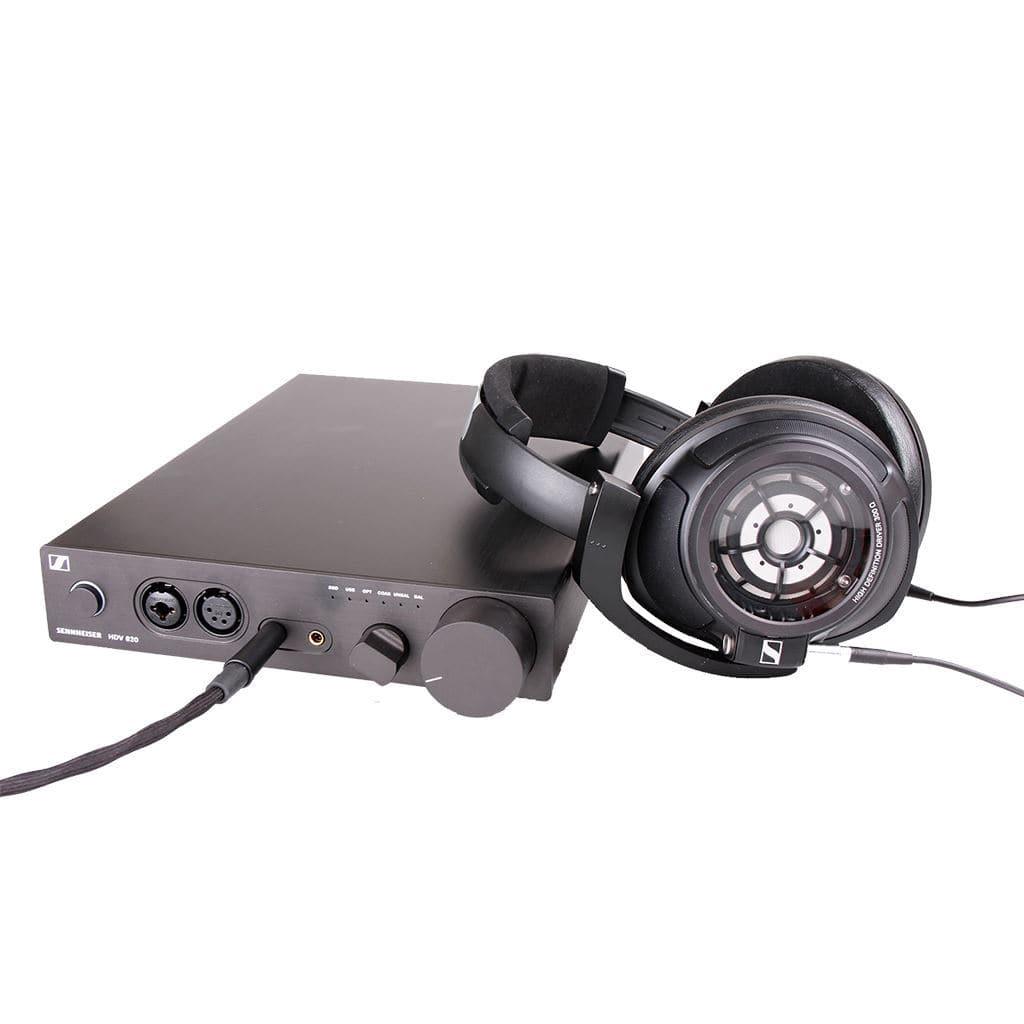 A pair of open-back Sennheiser headphones is connected to a black Sennheiser HDV 820 Headphone Amplifier with an ESS SABRE32 DAC, several ports, buttons, and a large volume knob, all set on a white surface.