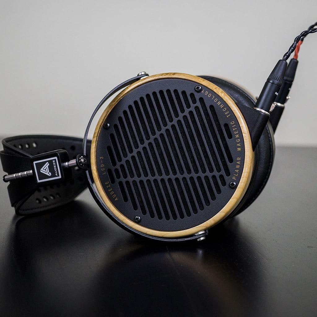 Close-up of premium Audeze LCD-3 Planar Magnetic Headphones in black and gold, showcasing a detailed grill design and audio cables—ideal for Hi-Fi listening—resting on a dark surface.