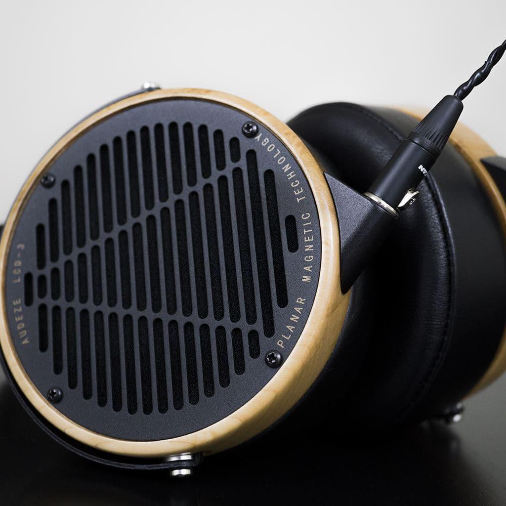 Close-up of Audeze LCD-3 headphones by Audeze, featuring wooden ear cups, black grilles with PLANAR MAGNETIC TECHNOLOGY and MODEL 603 text—ideal for Hi-Fi listening. A headphone cable is plugged into one ear cup.