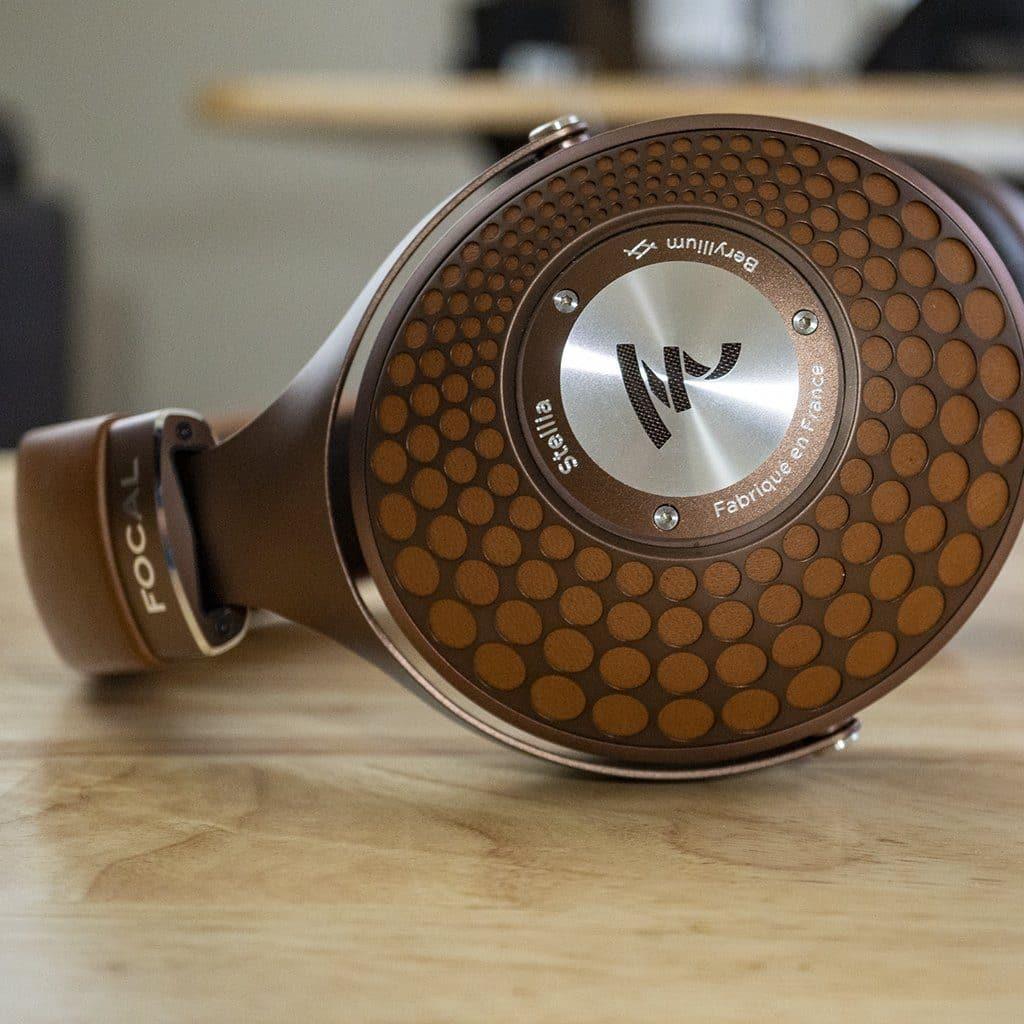 Close-up of brown Focal Stellia closed-back headphones on a wooden surface, displaying the earcup’s honeycomb grill and silver center plate with Focal logo, designed for excellent sound isolation.