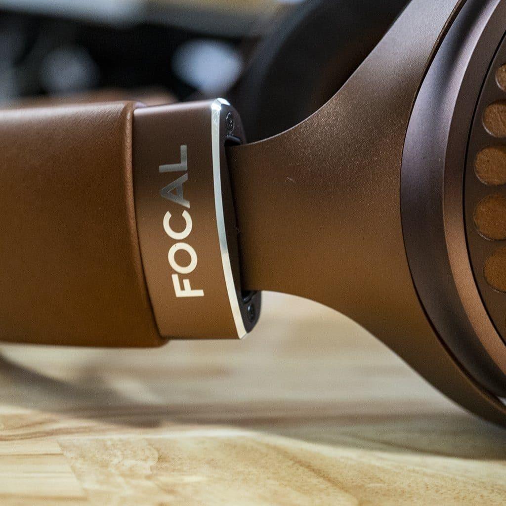 Close-up of brown Focal Stellia headphones on a wooden surface, showcasing the silver FOCAL logo near the ear cup and advanced beryllium dome drivers for outstanding sound quality.