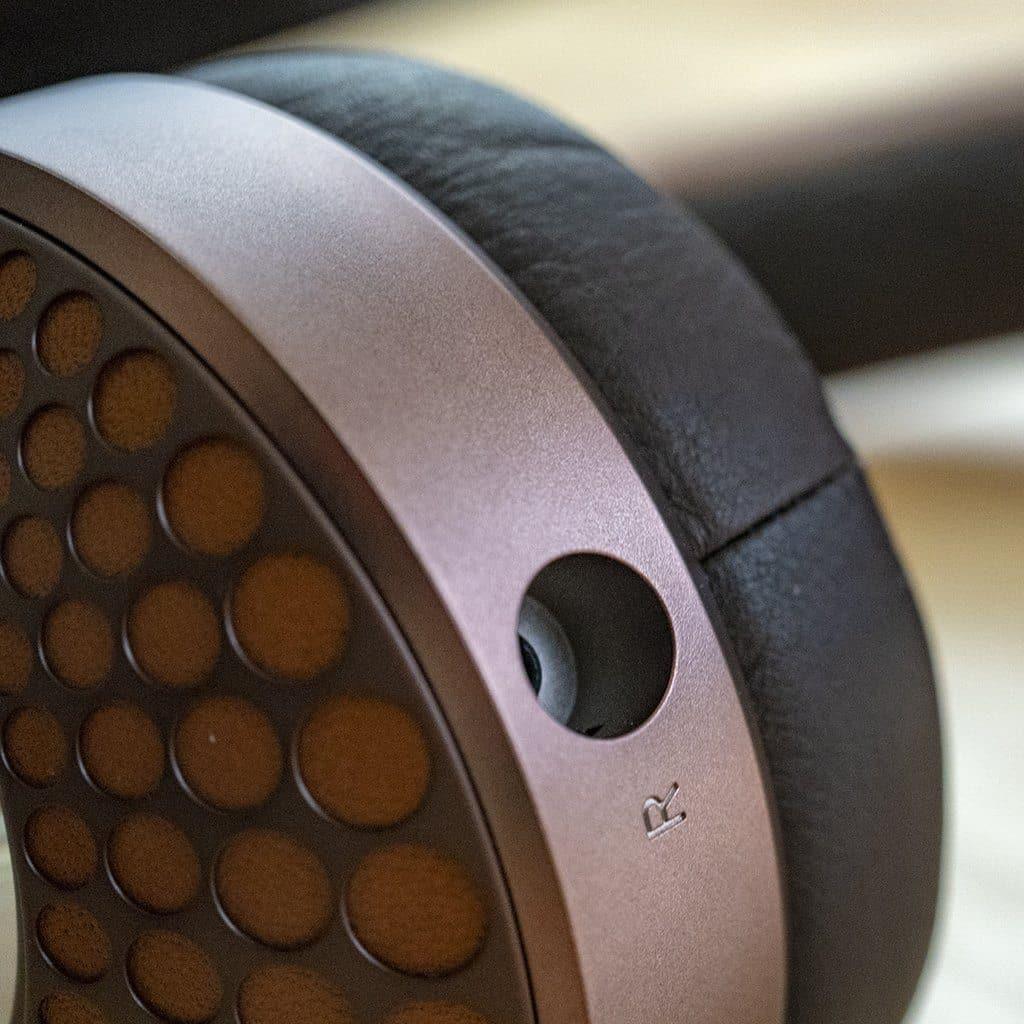 Close-up of Focal Stellia closed-back headphones with a brown metallic frame, black cushioned ear pad, dotted ear cup, and “R” for right. Features a beryllium dome driver by Focal for superior sound isolation and audio clarity.
