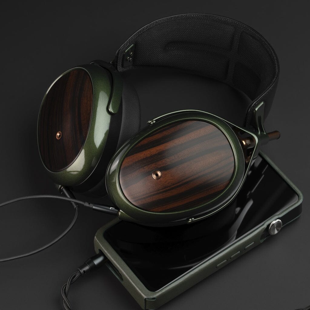The Meze Audio Strada closed-back dynamic headphones, featuring dark wood ear cups and green metallic details, sit beside a sleek dark green portable music player on a black surface, highlighting their refined tonal balance and elegant design.