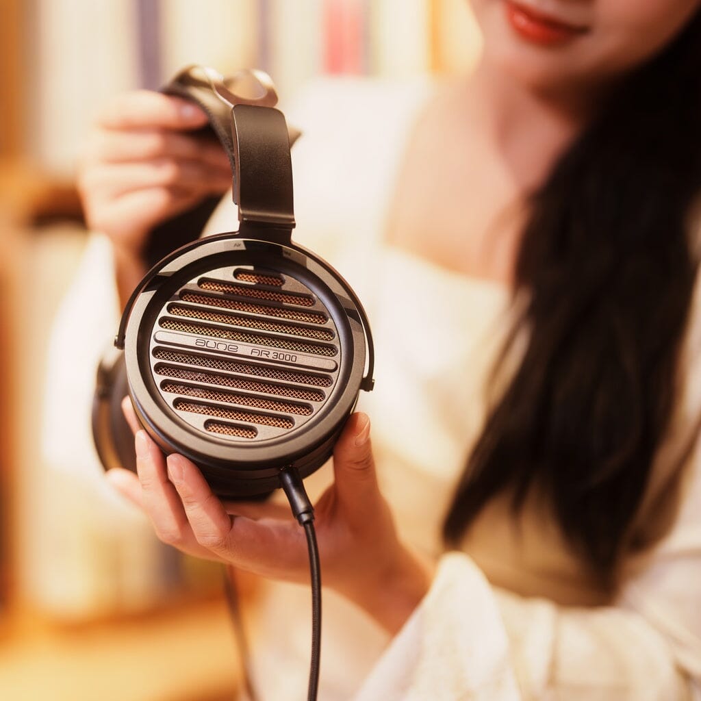 A person holds a pair of Aune Audio AR3000 headphones, showcasing the circular mesh grill.