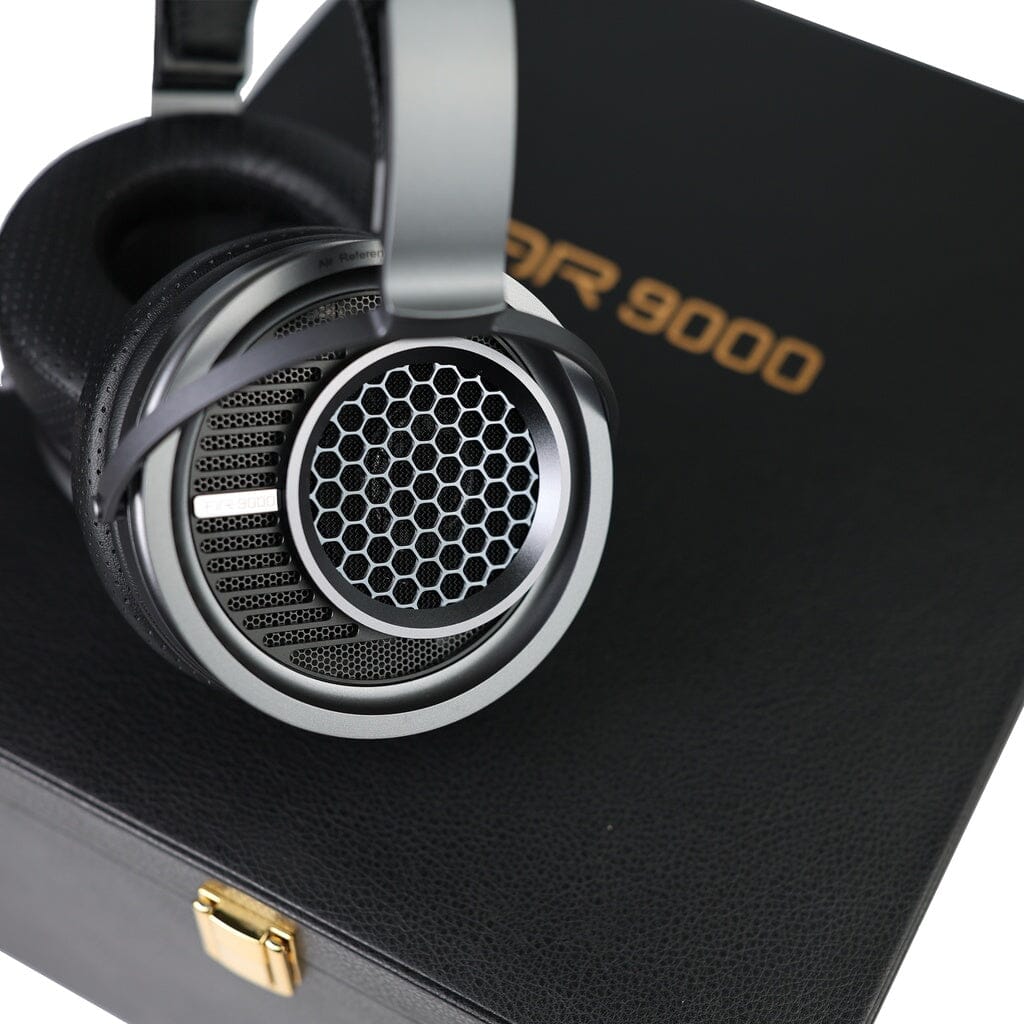 A pair of large, silver open-back headphones with a honeycomb grille rests on a black textured box labeled “Aune AR9000” in gold letters.