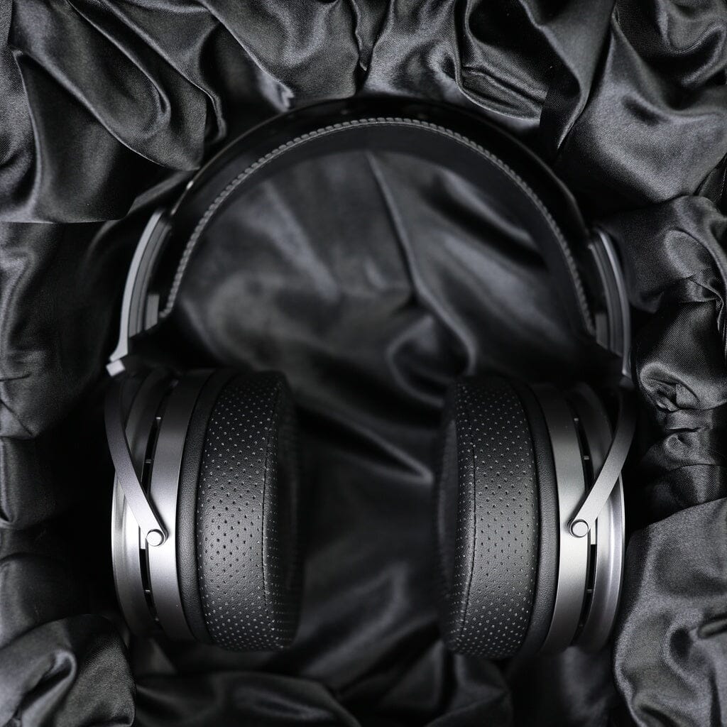 Black over-ear headphones, such as the Aune Audio Aune AR9000 Headphones, rest on crumpled black satin fabric, creating a luxurious and elegant backdrop that highlights the sleek and modern design of these open-back headphones.