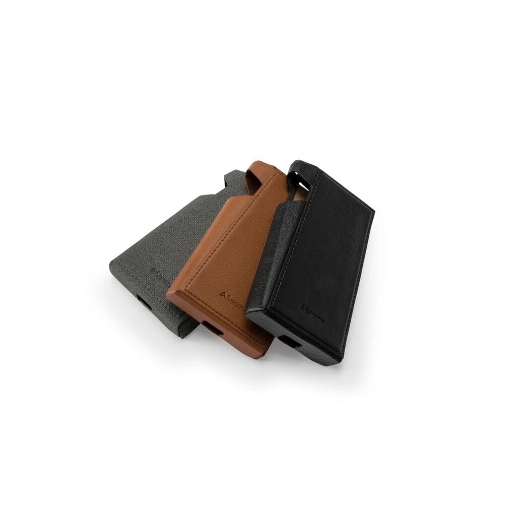 Three Astell & Kern A&norma SR35 Leather Protective Cases in gray, brown, and black overlap on a white background. Each case features top and side openings, subtle branding, and is crafted from premium LASKINA polyurethane fabric.
