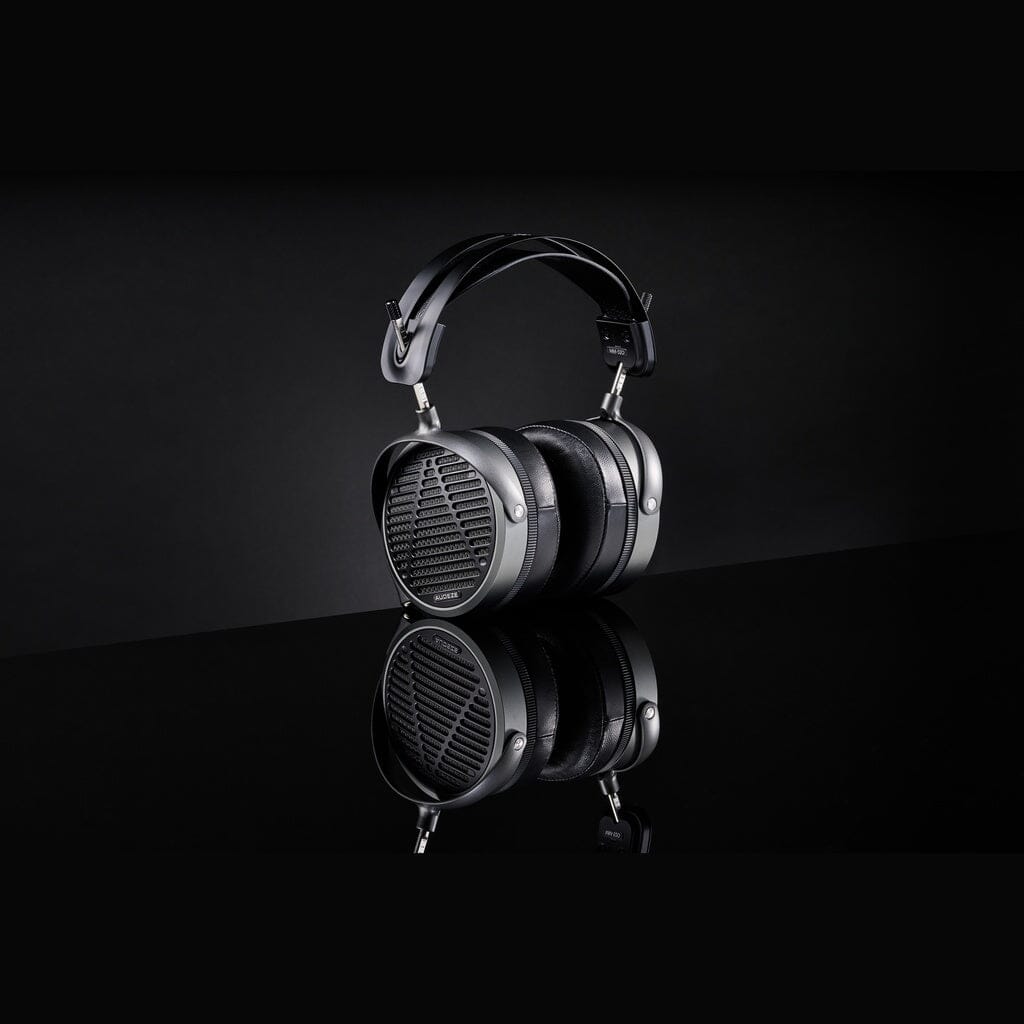 The Audeze MM-520 Headphones, featuring a sleek metal and leather design in black, are displayed against a matching background with their reflection visible. These advanced headphones use planar magnetic drivers for superior sound quality.