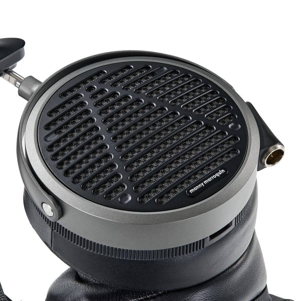 Close-up of Audeze MM-520 Headphones, large over-ear studio headphones with planar magnetic drivers, a metallic and black grille, padded ear cushions, and visible audio jack, resting on a black surface.