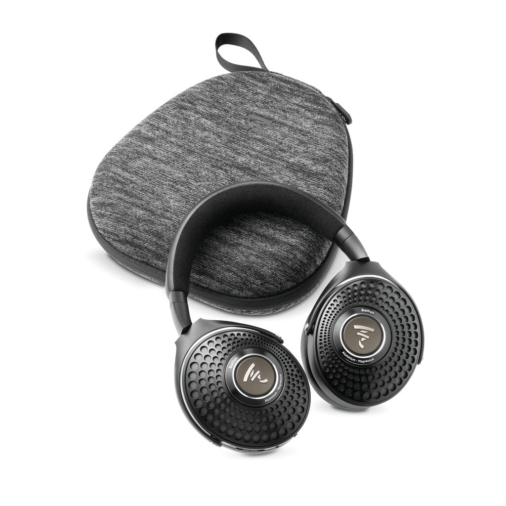 Black, over-ear Focal Bathys headphones by Focal, featuring wireless noise-canceling technology and a circular perforated design, are positioned in front of a gray zippered carrying case with a fabric texture and a small loop handle.