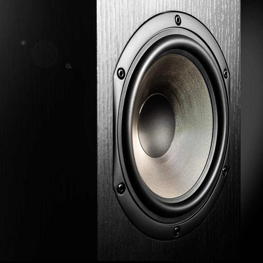 Close-up of the Cabasse JERSEY MC170 Floorstanding Speaker, showing its black 3-way design, metallic cone, textured surface, and visible screws on the wooden enclosure. The background is dark and blurred.