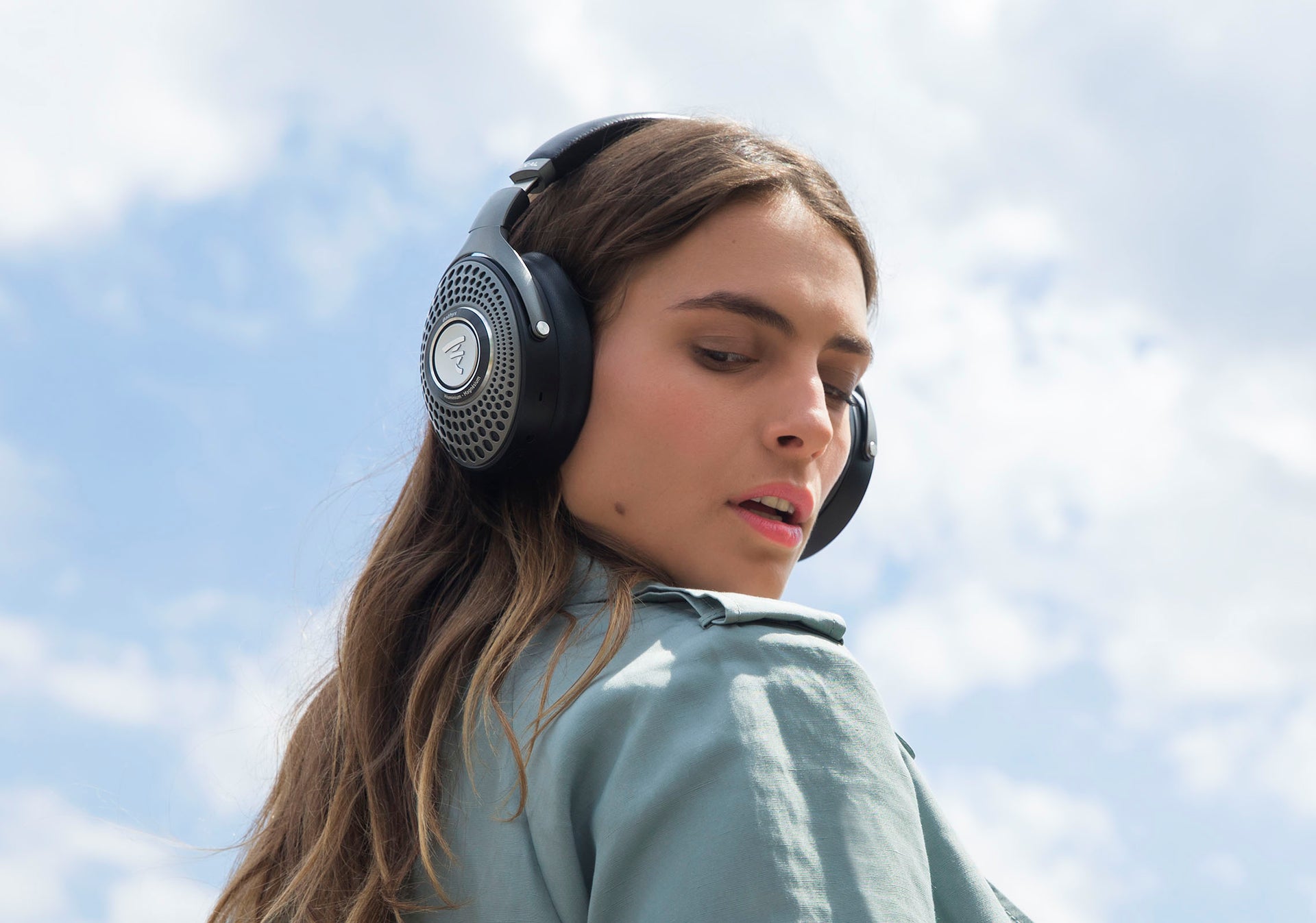 Woman wearing Focal Bathys wireless headphones with sky in background