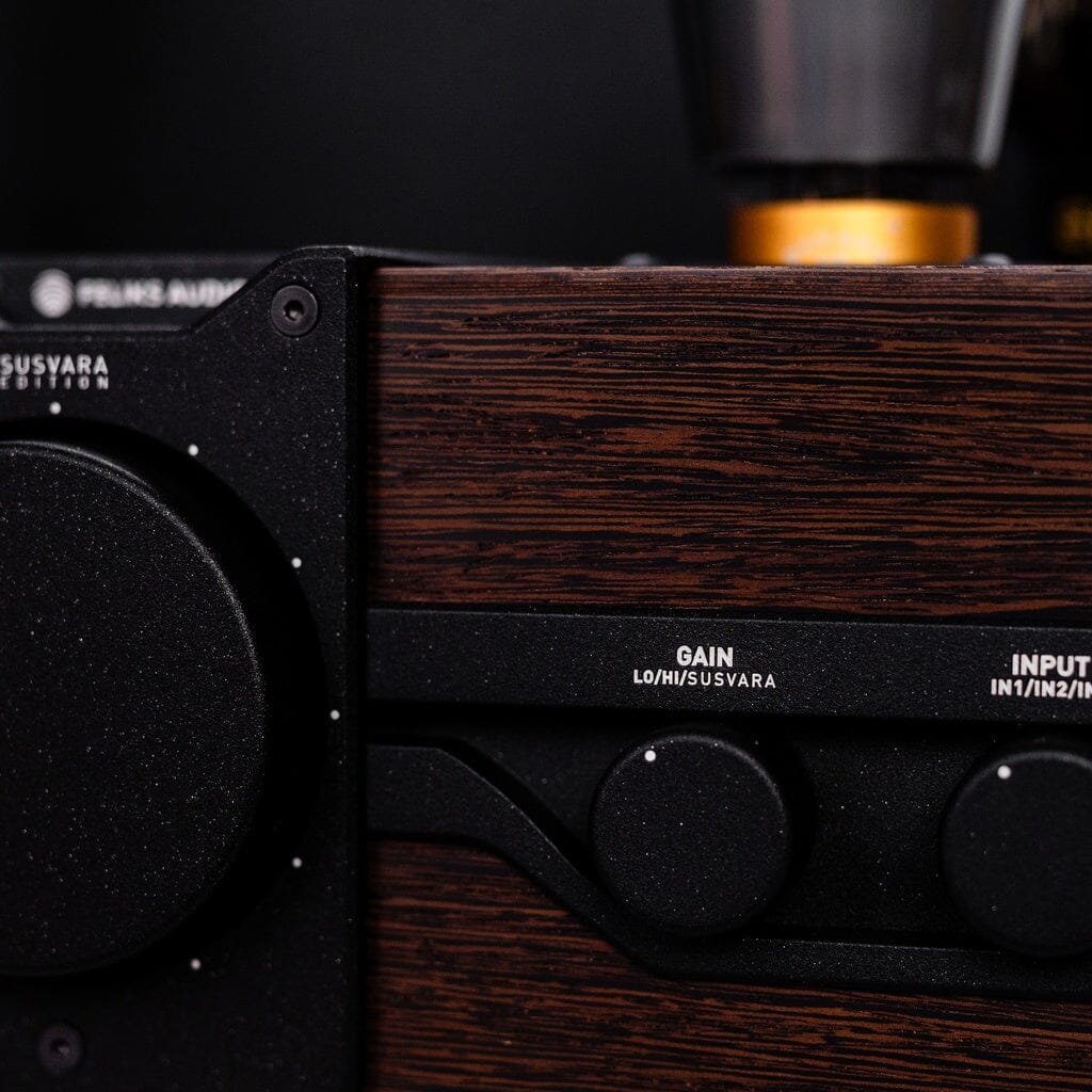 Close-up of the Feliks Audio Envy Susvara Edition headphone amplifier by Feliks Audio, featuring a wooden finish, black Gain and Input knobs, wood texture details, and part of a metallic component.