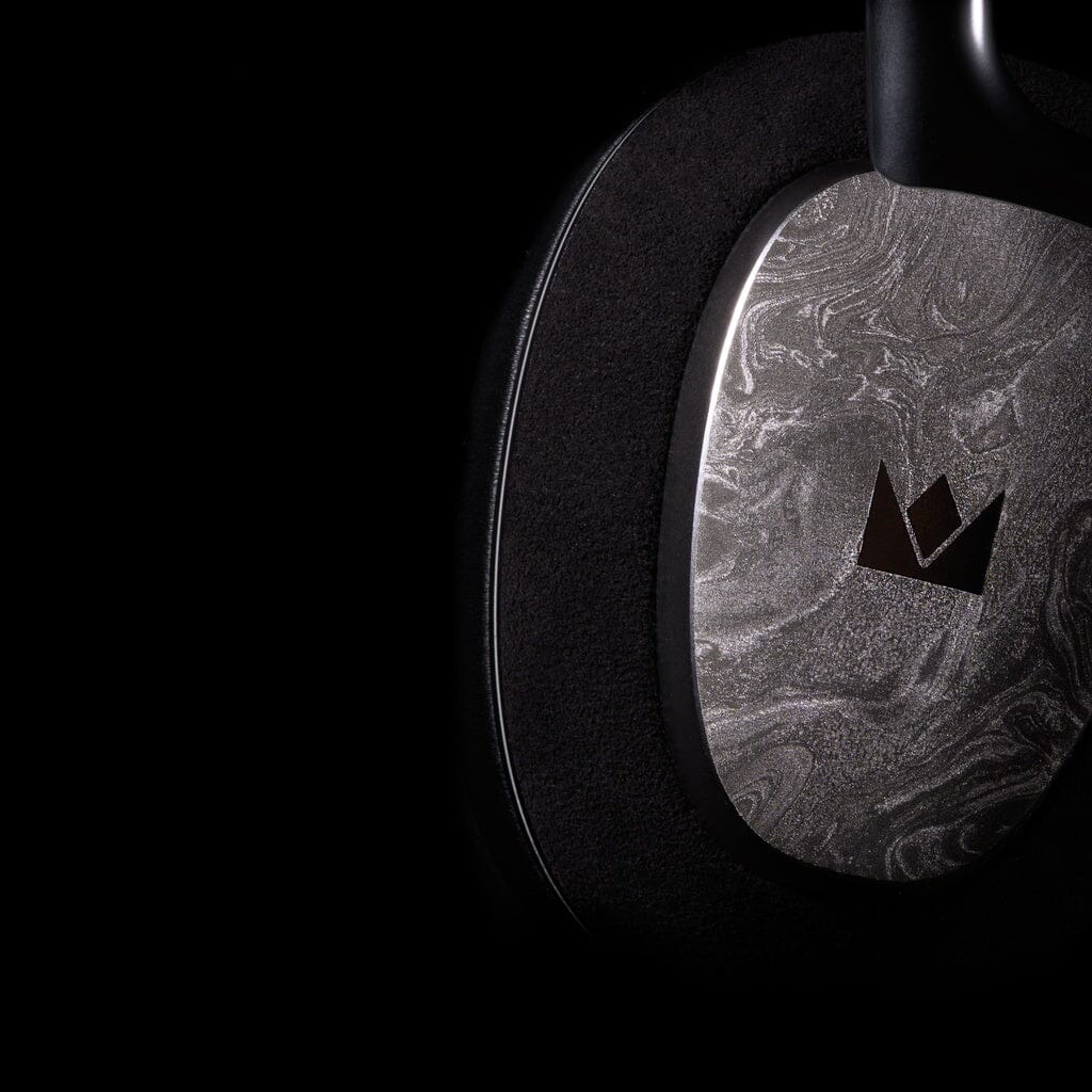 Close-up of a Noble Audio FoKus Artemis Wireless Headphones earcup, featuring a marbled gray pattern and black crown logo at the center, set against a dark background.