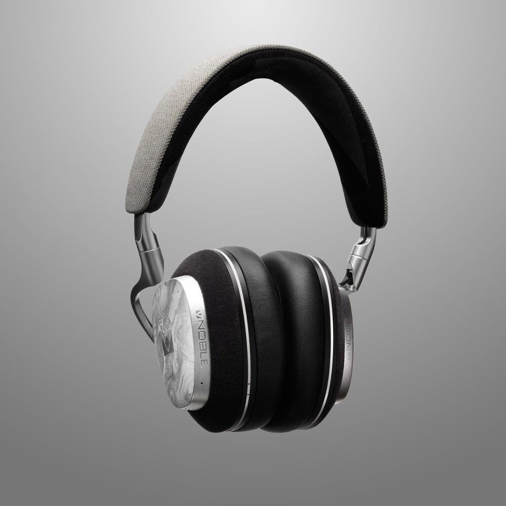 The Noble Audio FoKus Artemis Wireless Headphones by Noble Audio feature black cushioned ear cups, a gray and black padded headband, metallic silver accents, and active noise cancellation. Shown against a smooth gray gradient background.