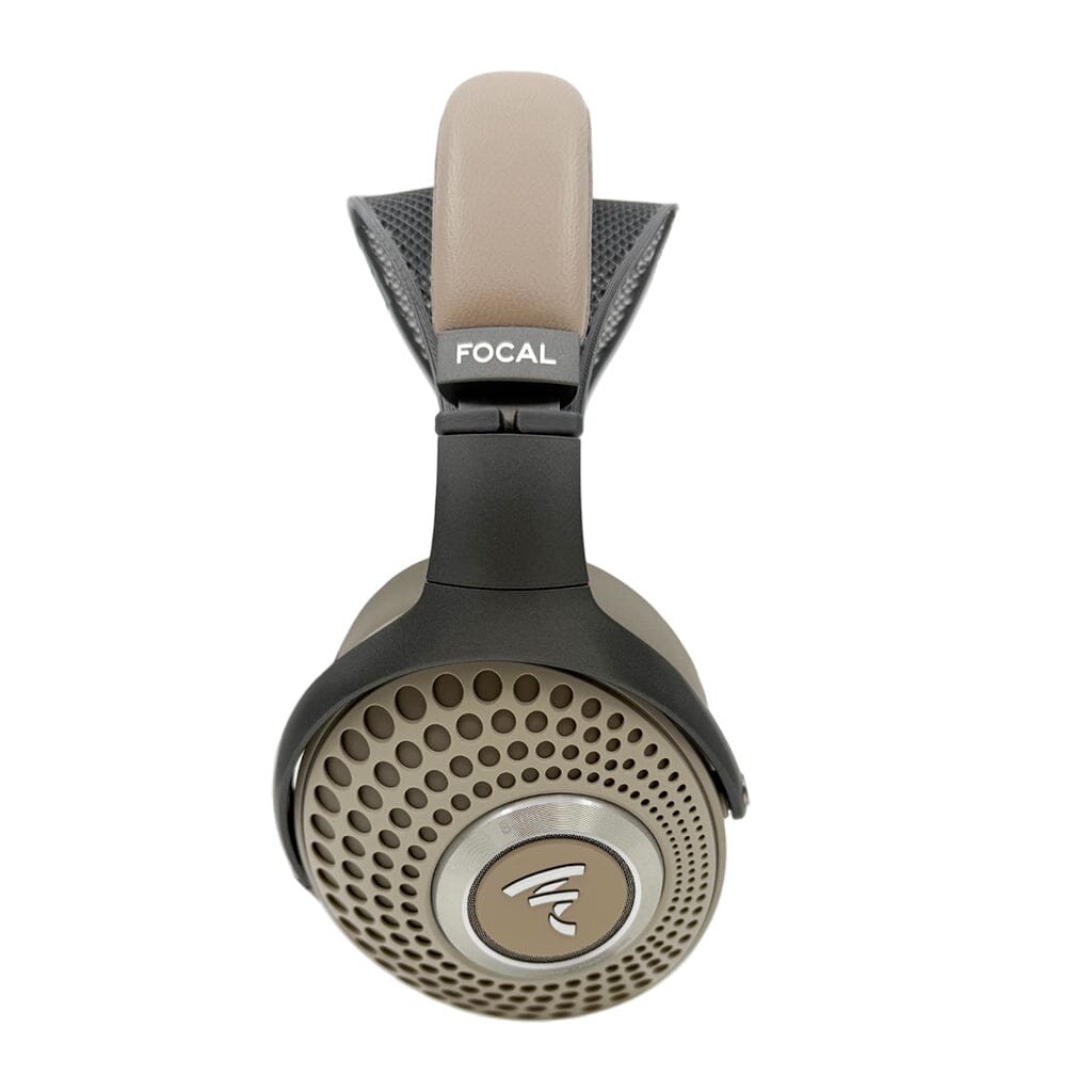 Tan and black over-ear Focal headphones shown from the side with perforated ear cups, a prominent Focal logo, padded headband, and a small Capra Comfort Strap by Capra Audio for added comfort.