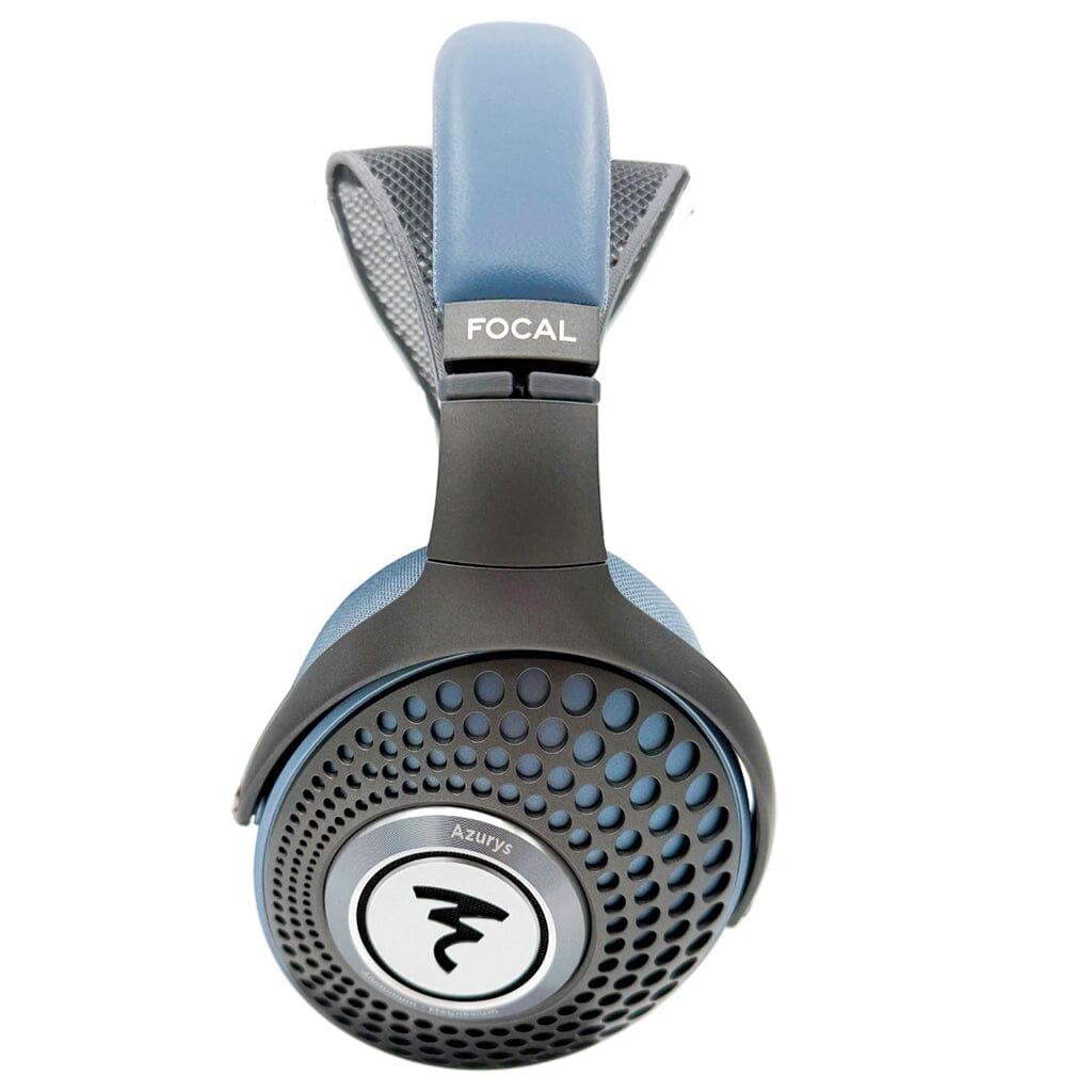 A close-up of Focal Azurys over-ear headphones shows the blue padded headband upgraded with the Capra Audio Comfort Strap (Small) for added comfort and a perforated black ear cup featuring the Focal logo.