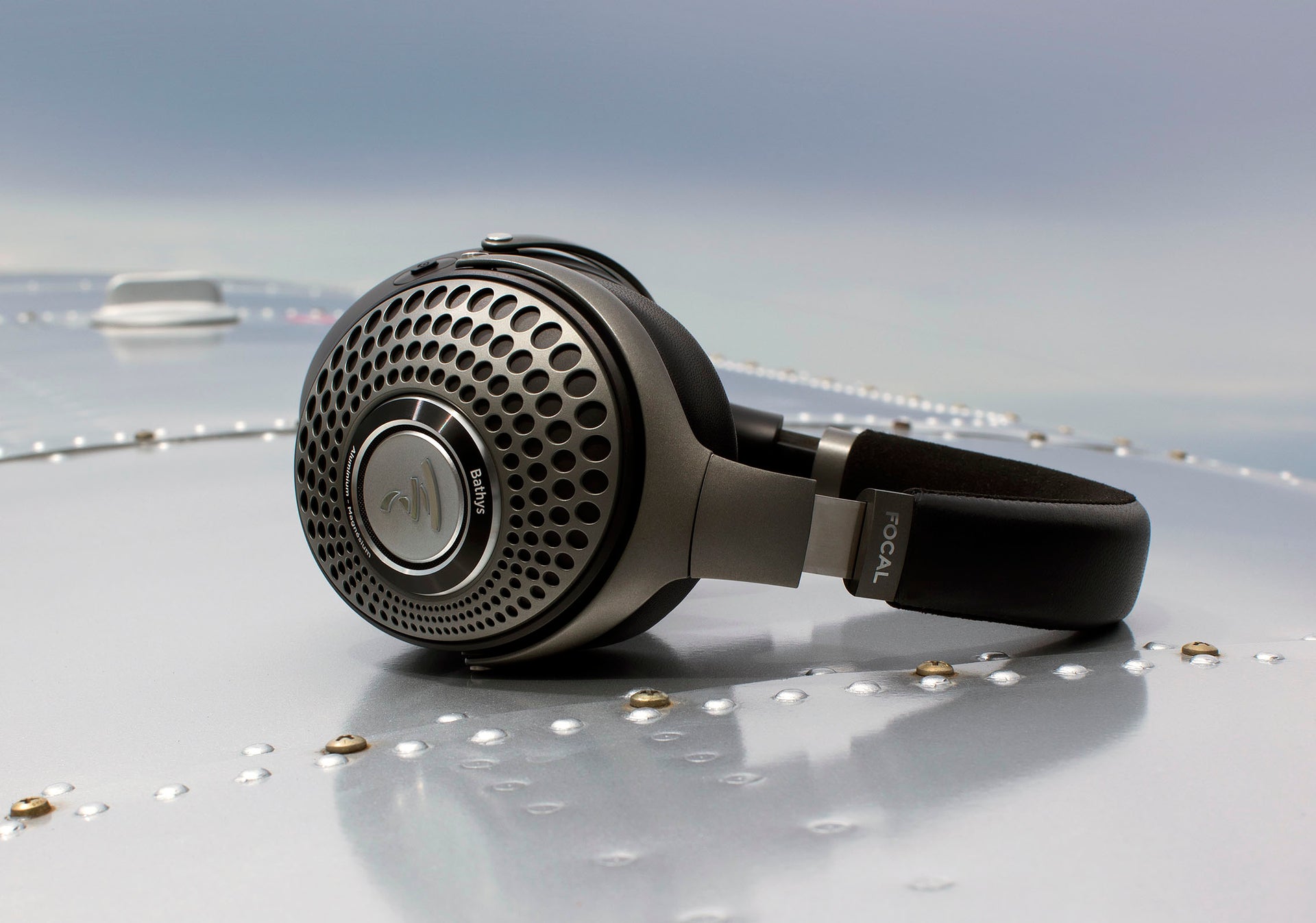 Focal Bathys wireless noise-cancelling audiophile headphones on a riveted metal surface.