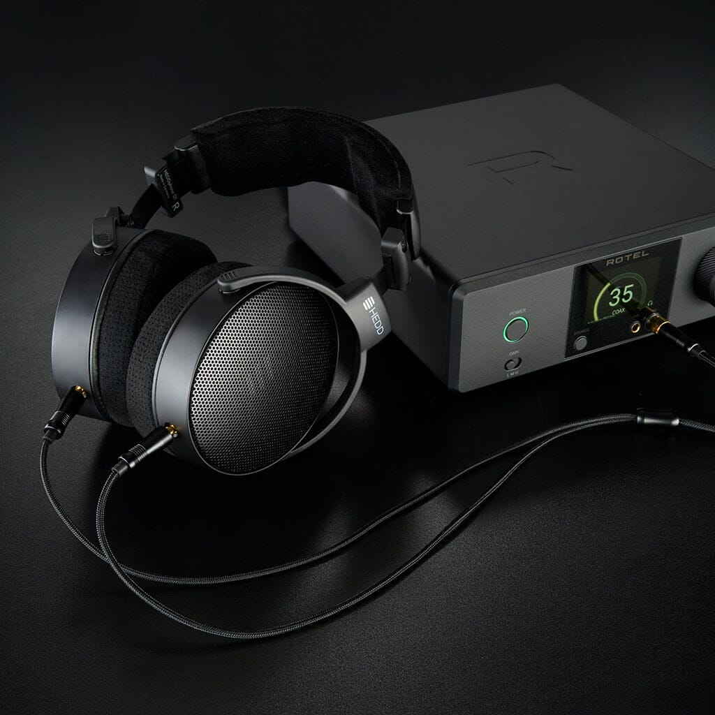 A pair of black HEDD Audio HEDDphone D1 headphones is connected to a black Rotel audio amplifier on a dark surface, with the green-lit volume indicator showing 35.