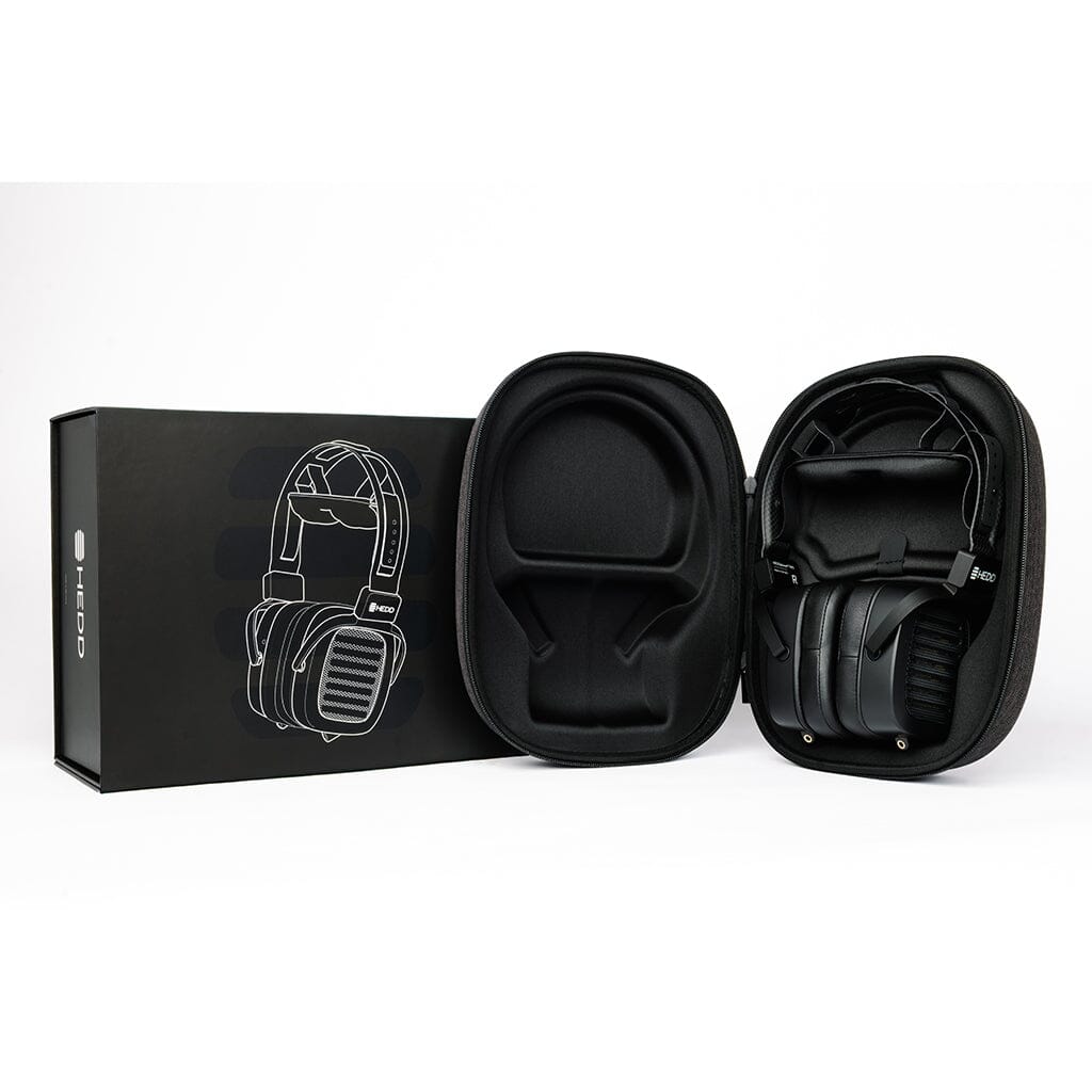 The HEDD Audio HEDDphone TWO UNPLUGGED Edition reference headphones with an AMT driver are displayed in an open hard case, next to a black HEDD Audio box featuring a line drawing of the headphones.