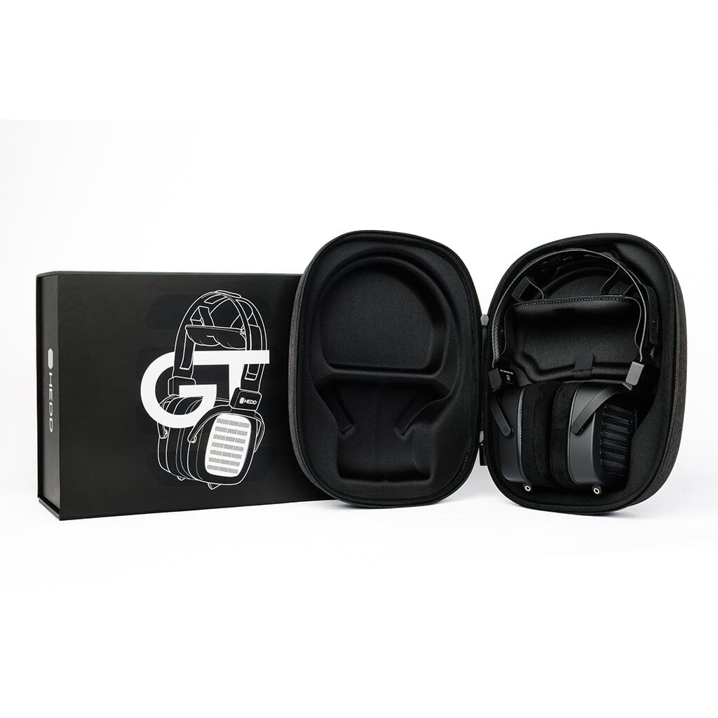 A pair of black HEDD Audio HEDDphone TWO GT UNPLUGGED Edition over-ear headphones is shown in an open hard-shell case beside a black box featuring a white outline illustration of the headphones.