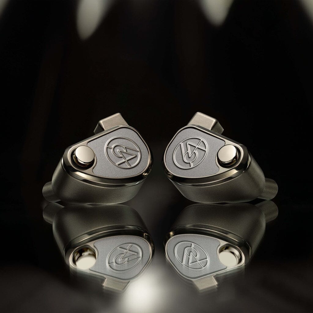 A pair of 64 Audio TWELVE Ti In-Ear Headphones by 64 Audio, featuring circular buttons and engraved logos, are placed side by side on a reflective black surface.
