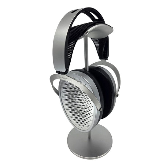 A pair of silver and black Hifiman over-ear headphones with mesh ear cups, featuring the Capra Audio Capra Comfort Strap for support, rests on a sleek metallic stand against a white background.