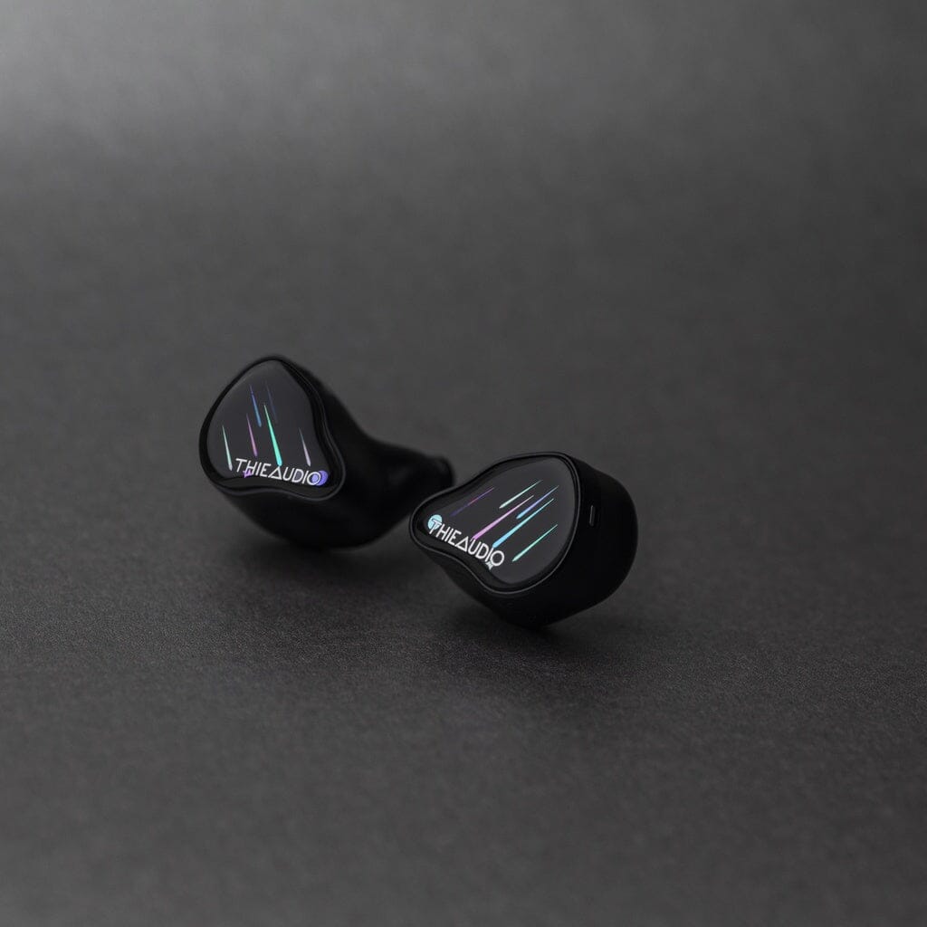A pair of Thieaudio Monarch MKIV In-Ear Headphones with a glossy black finish and colorful lines rests on a smooth, dark surface, featuring an adjustable tuning switch for personalized sound.
