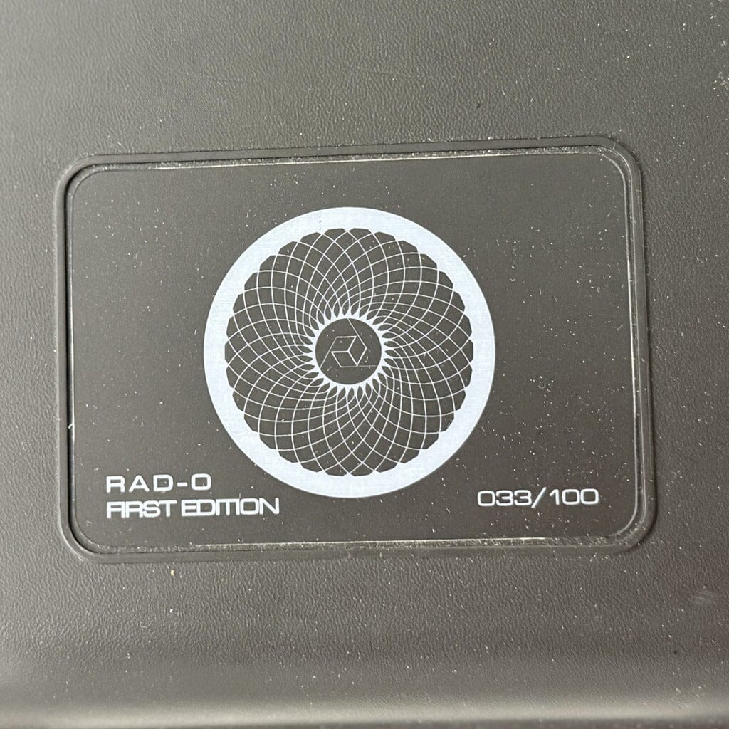 A black label featuring a geometric white circular pattern, with the text "RAD-0 FIRST EDITION" emphasizing its status within the acclaimed Rosson Audio Design RAD-0 Headphones line, and "33/100" displayed in the bottom right corner.