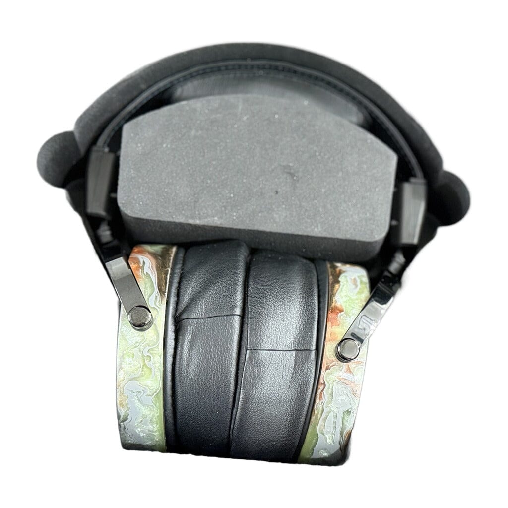 A close-up of Rosson Audio Design RAD-0 Headphones - Open Box - Clearance - 33 shows the black planar magnetic headphones with padded ear cups and a foam headband, featuring a marbled green and tan pattern on the outer ear cup surfaces. The background is white. This is an open-box item from Rosson Audio Design.