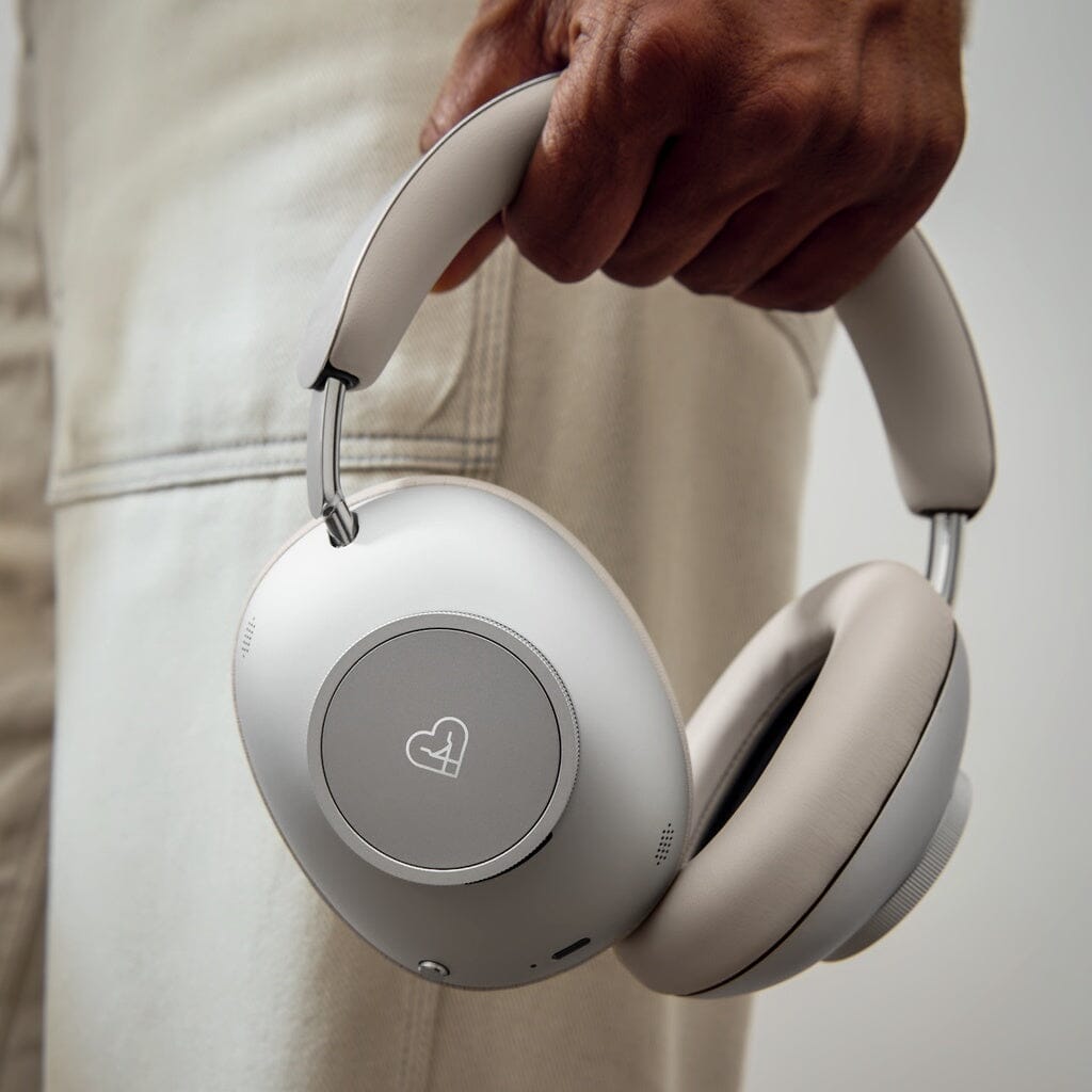 A person holds the Loewe Leo Wireless Headphones by Loewe, featuring a heart-shaped logo on the ear cup, standing against a neutral background.