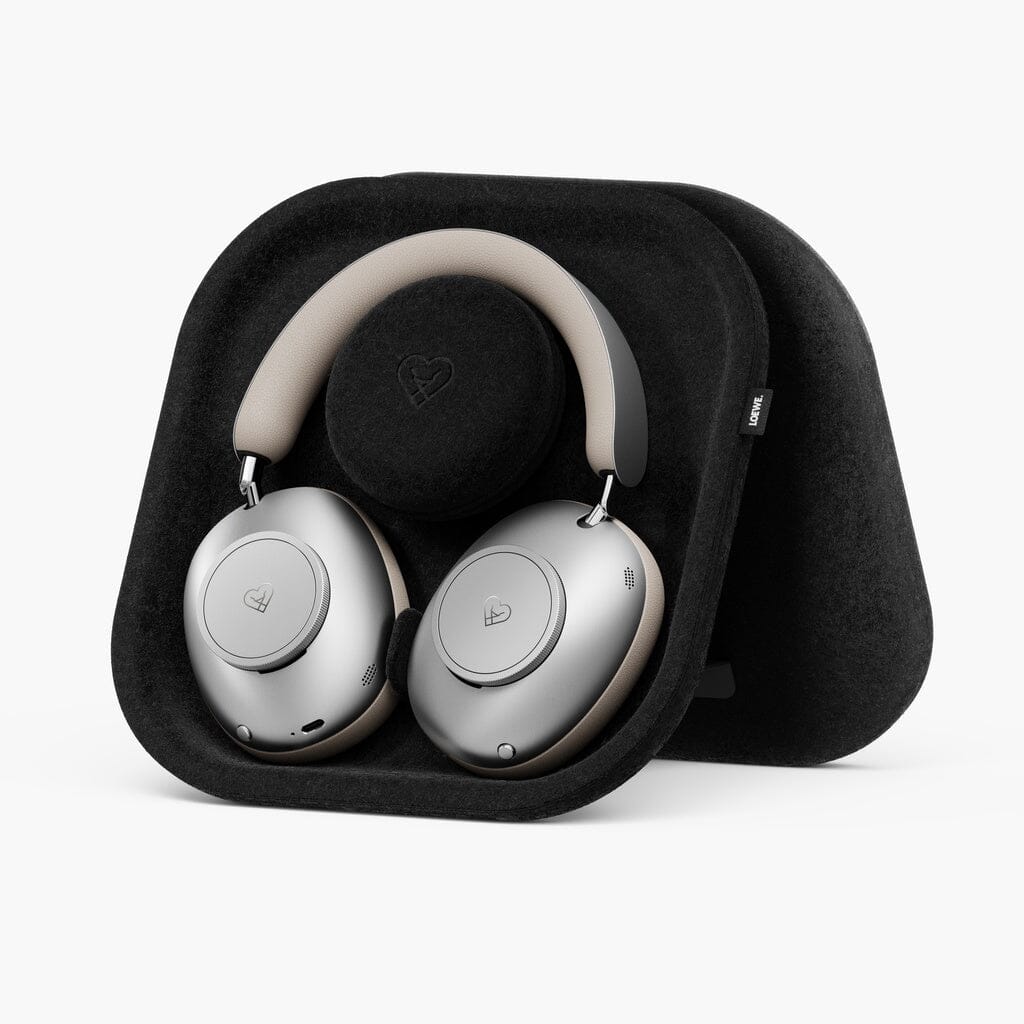 The Loewe Leo Wireless Headphones by Loewe feature a sleek silver over-ear design with plush beige padding on the headband, elegantly nestled in a contoured black carrying case. Both the ear cups and the case display a subtle heart logo. These premium wireless headphones deliver personalized sound and adaptive noise cancellation, all presented in a modern, minimalistic aesthetic.
