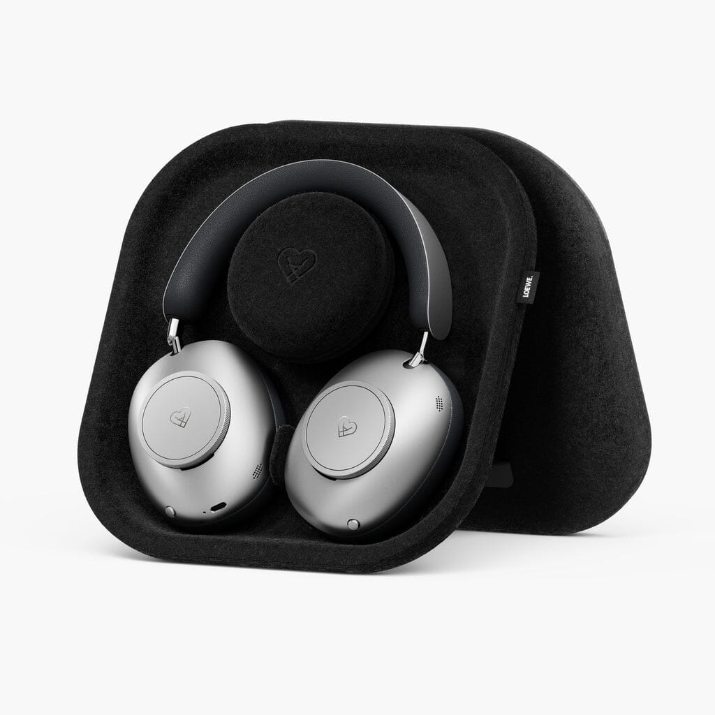 Loewe Leo Wireless Headphones in silver, equipped with adaptive noise cancellation for an immersive listening experience, are displayed resting in a black, square-shaped, felt-lined case. Both the headphones and the case feature a small heart-shaped Loewe logo. The background is plain white.