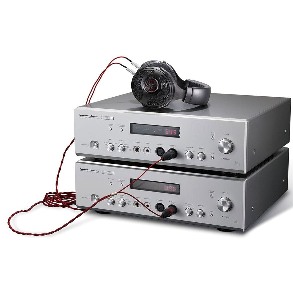 Two silver Luxman P-100 Centennial Headphone Amplifiers are stacked, connected with red cables and topped with high-fidelity headphones, creating a stylish Luxman setup for superb sound quality.