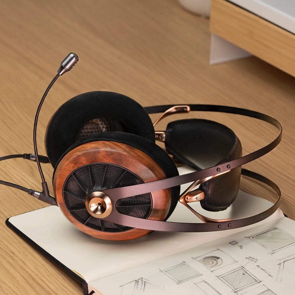 The Meze Audio Boom Mic by Meze, a stylish gaming headset with a wooden finish and detachable mic, rests on an open sketchbook with architectural drawings on a wooden desk.