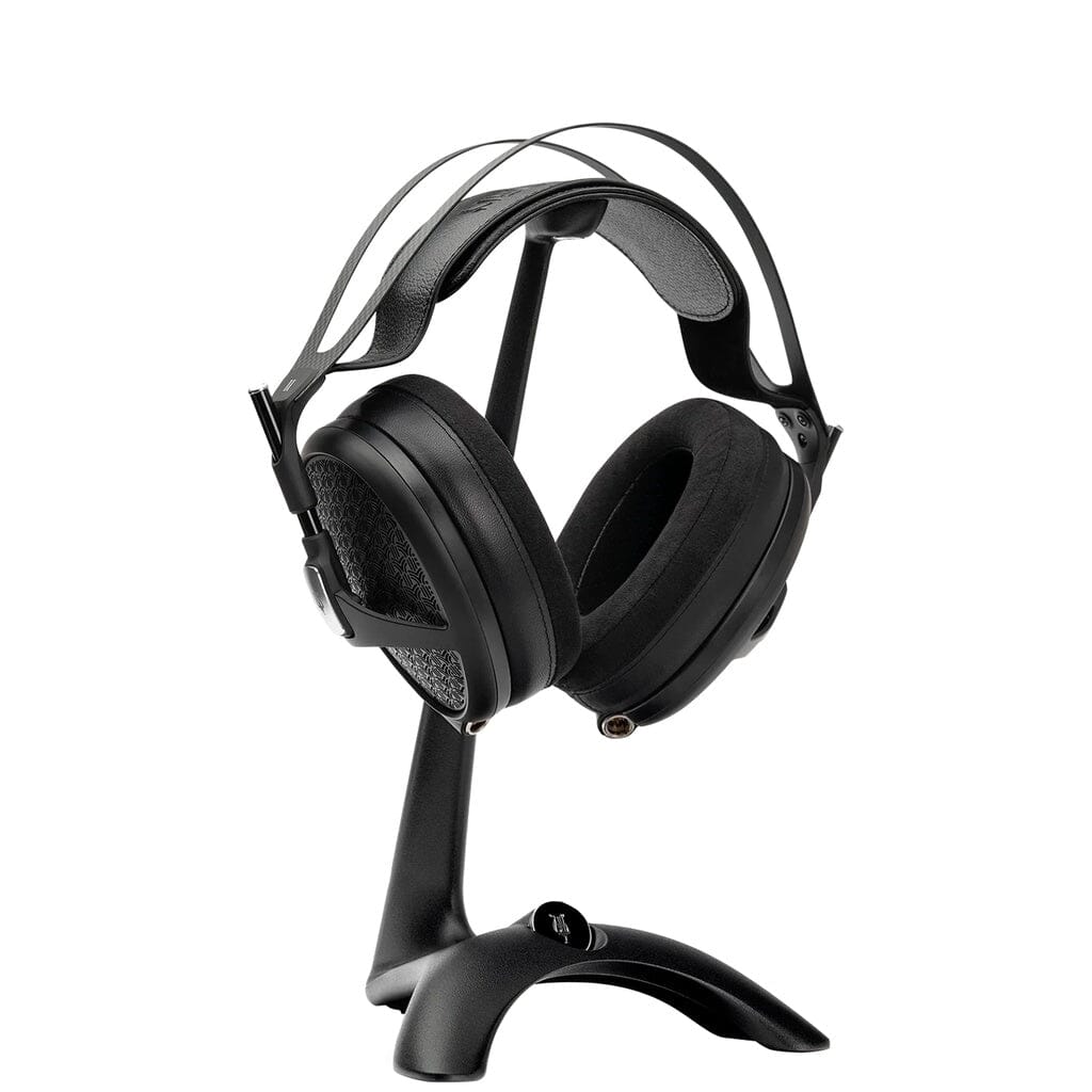 A pair of black over-ear headphones with a padded headband sits on the Meze Audio Manta Headphone Stand by Meze, featuring cable management, displayed against a white background.