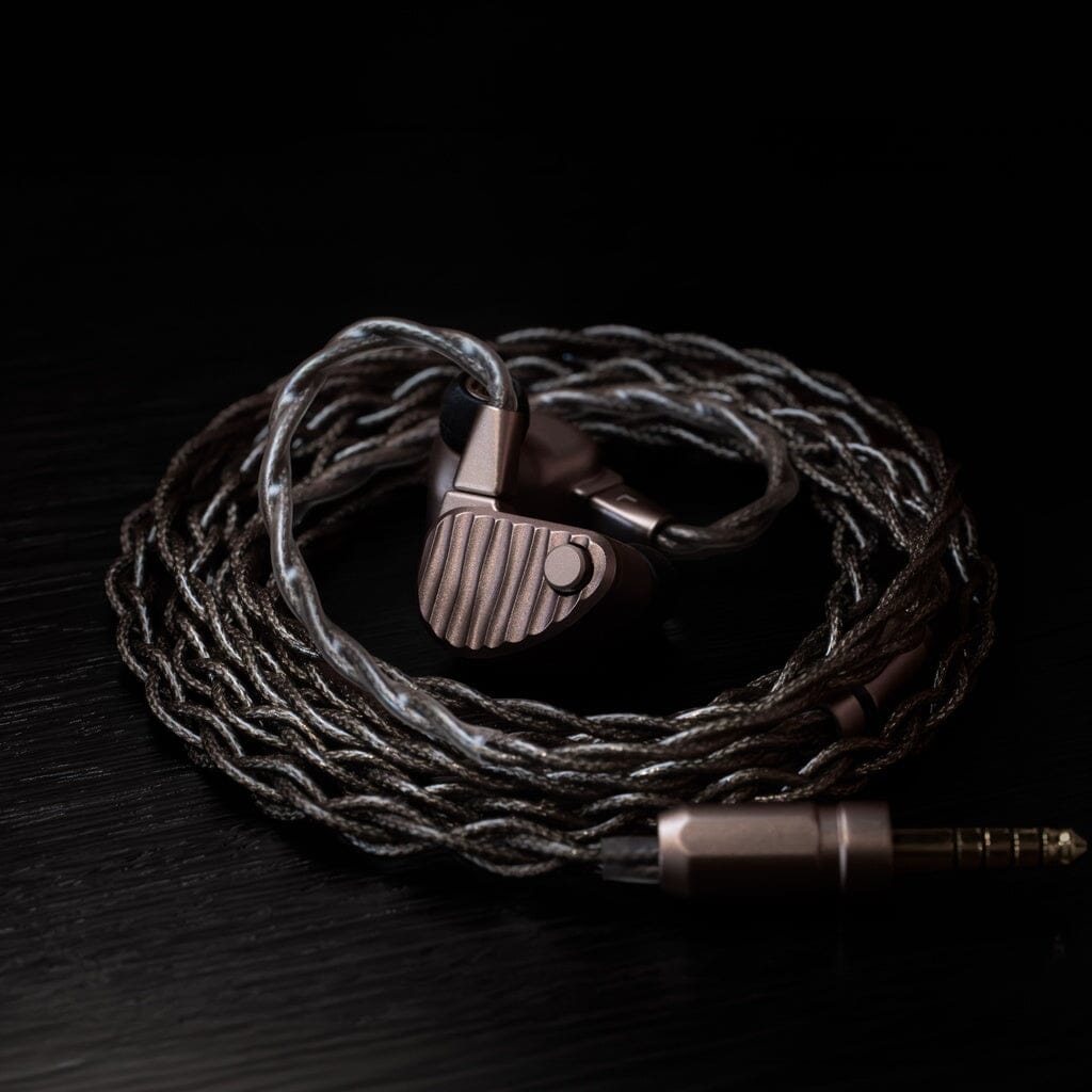 The 64 Audio Ocean In-Ear Headphones by 64 Audio, featuring copper-colored earpieces with a grooved metallic texture and a twisted cable, are coiled neatly on a dark surface. A 3.5mm audio jack lies beside the flagship universal IEMs, renowned for their sophisticated hybrid driver design.